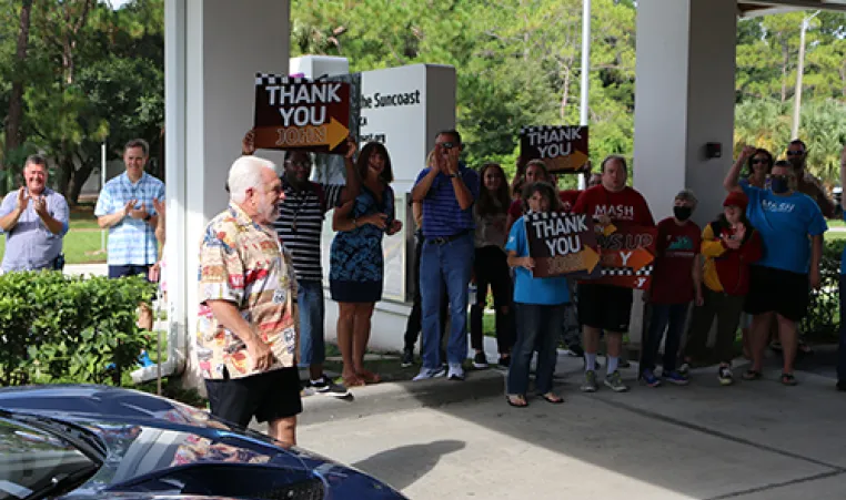 John Geigle walks into crowd holding thank you signs at namesake YMCA