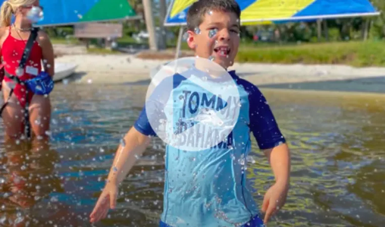 lifeguard standing in lake watching over children. focus of photo is child knee deep in lake, splashing, having fun. click the image to play the video