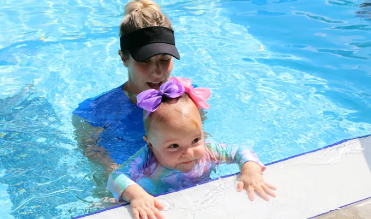 A swim instructor and baby at the edge of an outdoor pool. The FLOAT program teaches young children how to float if they fall into a body of water.