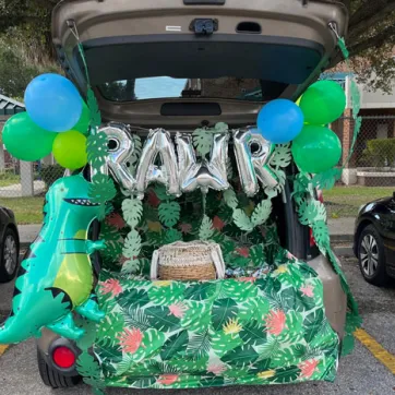 Open car trunk decorated in dinosaur in the jungle theme in a parking lot at a Trunk or Treat event.